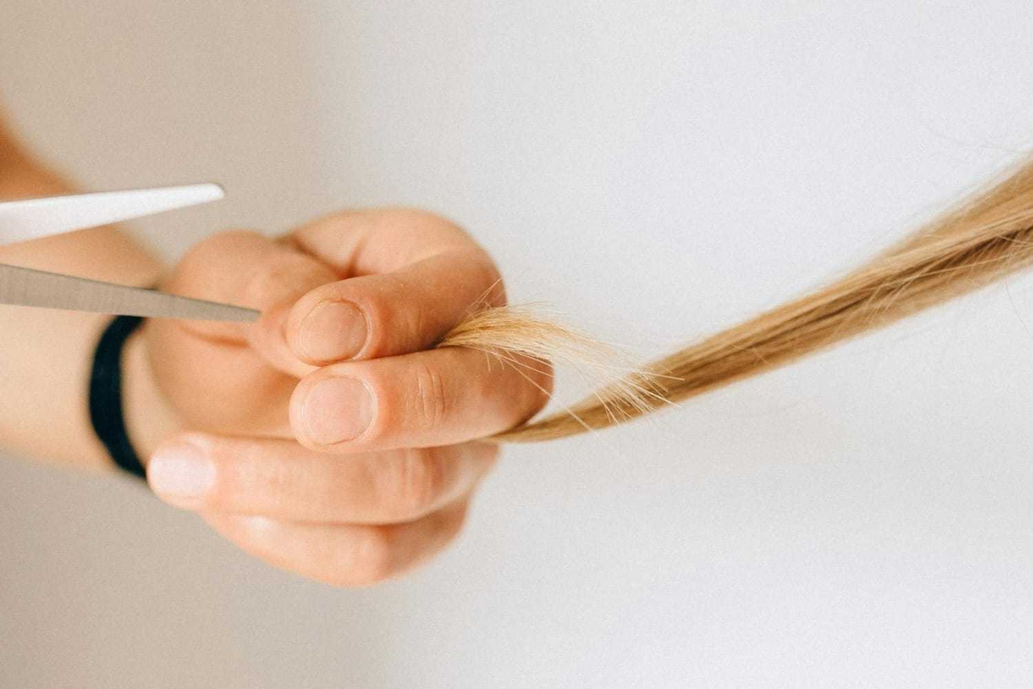 Person trimming a strand of blonde hair with scissors.