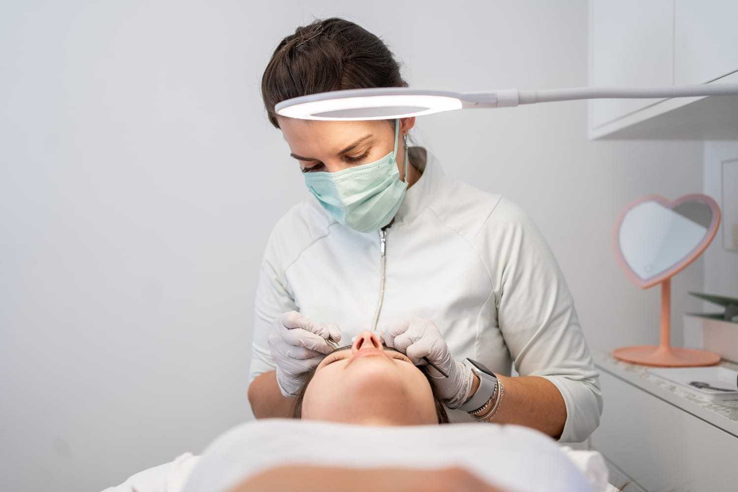 Esthetician performing a facial treatment under a bright lamp.